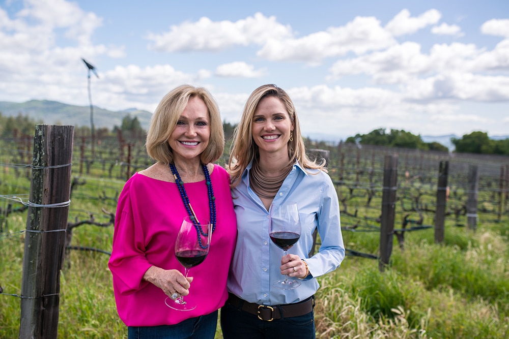 Kathryn Hall and daughter Jennifer in a vineyard with glasses of red wine